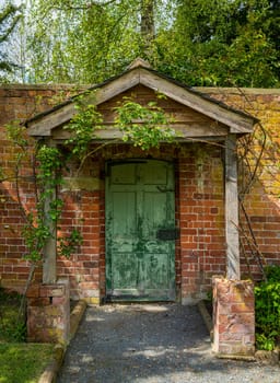 Painted green door and wooden porch as entrance to walled garden made with brick