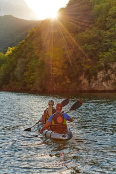 A young couple enjoying an idyllic kayak ride in the middle of a beautiful river surrounded by forest greenery in sunset time.