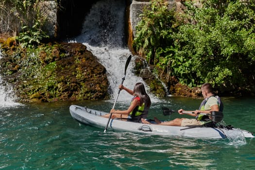 A young couple enjoying an idyllic kayak ride in the middle of a beautiful river surrounded by forest greenery.