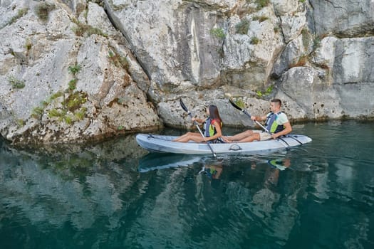 A young couple enjoying an idyllic kayak ride in the middle of a beautiful river surrounded by forest greenery.