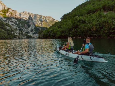 A young couple enjoying an idyllic kayak ride in the middle of a beautiful river surrounded by forest greenery.