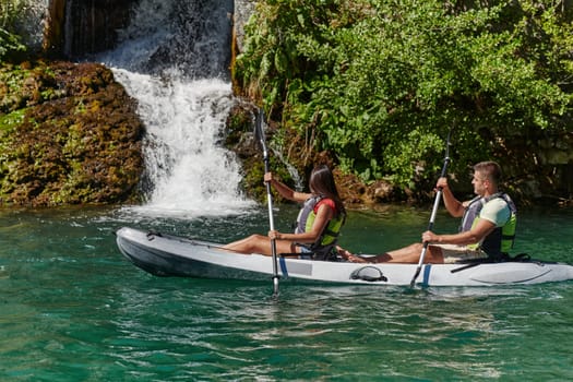 A young couple enjoying an idyllic kayak ride in the middle of a beautiful river surrounded by forest greenery.