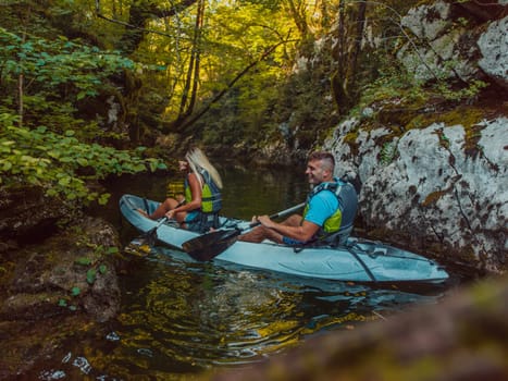 A young couple enjoying an idyllic kayak ride in the middle of a beautiful river surrounded by forest greenery.