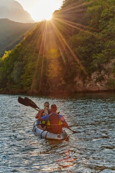 A young couple enjoying an idyllic kayak ride in the middle of a beautiful river surrounded by forest greenery in sunset time.