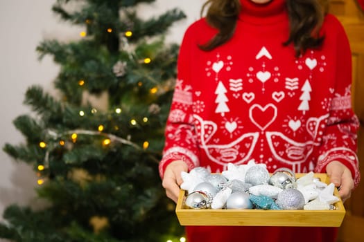 Female hands hold a tray in which there are a lot of Christmas tree toys. Christmas tree decoration process. New Year Christmas. 2022 year of the tiger