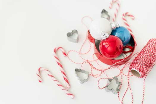 Christmas candies, along with cookie cutters, Christmas tree toys and red thread for gift wrapping, lie on a white table. Selective focus, noise. Christmas and New Year 2023-2024