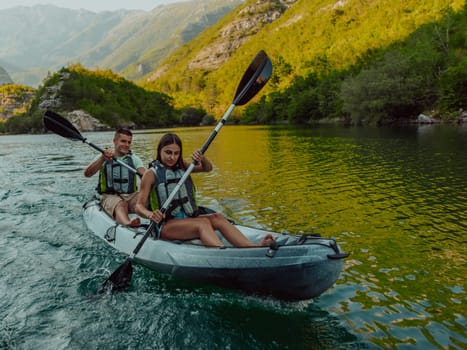 A young couple enjoying an idyllic kayak ride in the middle of a beautiful river surrounded by forest greenery.