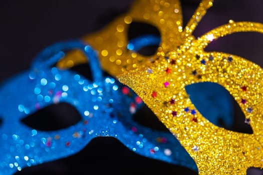 Yellow and blue shiny venetian carnival mask isolated on black background. New Year's party, hide your face. Close-up