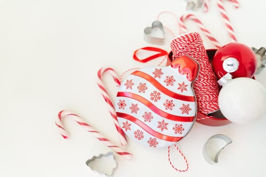 Christmas candies, along with cookie cutters, Christmas tree toys and red thread for gift wrapping, lie on a white table. Selective focus, noise. Christmas and New Year 2023-2024. Place for an inscription