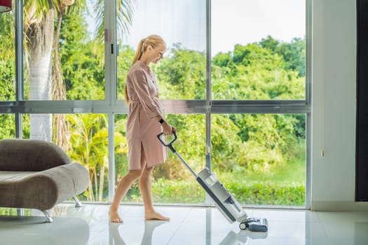 Young pregnant woman enjoys cleaning her house. Easy cleaning with a wireless vacuum cleaner. Pregnant woman cleaning floor with handheld vacuum cleaner. Modern easy cleaning.