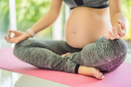 Young pregnant woman doing yoga exercises and meditating at home or yoga studio. Health care, mindfulness, relaxation and wellness concept.