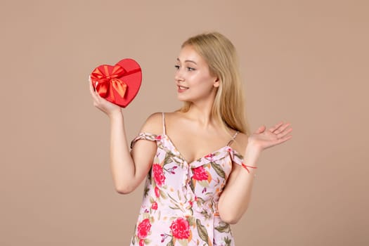 front view young female holding red heart shaped present on brown background feminine sensual money march woman shopping horizontal marriage