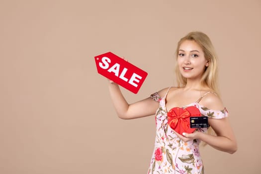 front view young female holding red present sale nameplate and bank card on brown background money march horizontal feminine equality sensual shopping