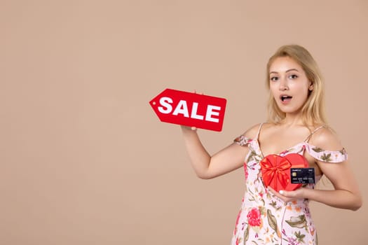 front view young female holding red present sale nameplate and bank card on brown background money march horizontal feminine equality sensual shopping woman