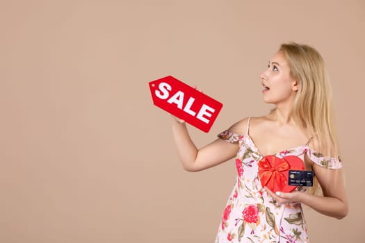 front view young female holding red present sale nameplate and bank card on brown background money march horizontal woman equality sensual shopping