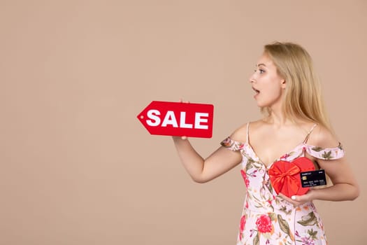 front view young female holding red present sale nameplate and bank card on brown background money march horizontal woman feminine equality sensual