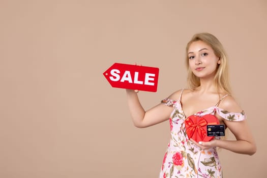 front view young female holding red present sale nameplate and bank card on brown background money march horizontal woman feminine equality shopping