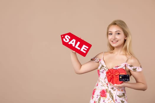 front view young female holding red present sale nameplate and bank card on brown background money march horizontal woman feminine sensual shopping