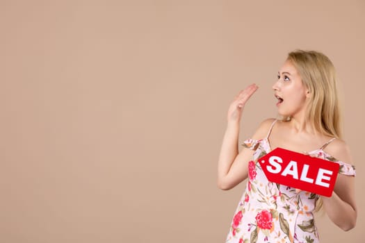 front view young female holding red sale nameplate on brown background woman money march horizontal sensual shopping equality feminine