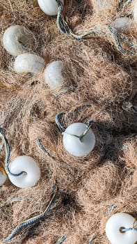 Fishing net with white floats and ropes lies on ground, top view, vertical frame