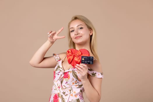 front view young female posing with red heart shaped present and bank card on brown background feminine march woman sensual horizontal equality