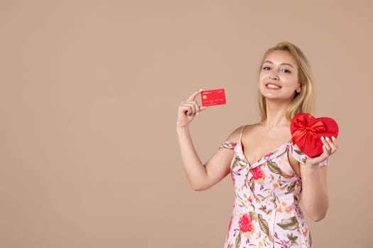 front view young female posing with red heart shaped present and bank card on brown background feminine money march horizontal equality woman sensual