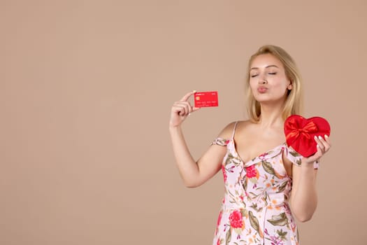 front view young female posing with red heart shaped present and bank card on brown background feminine money march horizontal woman sensual