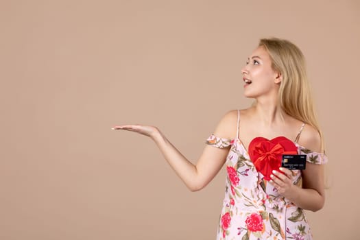 front view young female posing with red heart shaped present and bank card on brown background feminine money march sensual horizontal equality