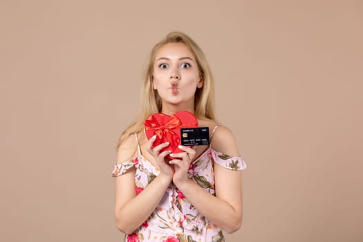 front view young female posing with red heart shaped present and bank card on brown background feminine money march woman sensual equality
