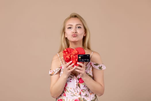 front view young female posing with red heart shaped present and bank card on brown background feminine money march woman sensual horizontal