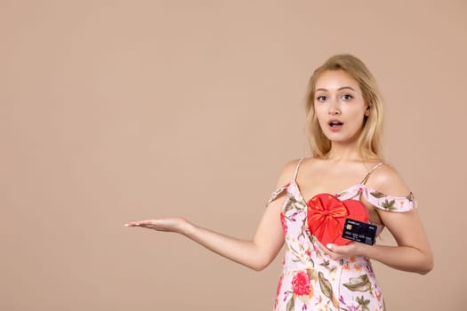 front view young female posing with red heart shaped present and bank card on brown background money march woman feminine equality sensual