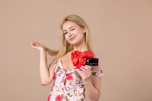 front view young female posing with red heart shaped present and bank card on brown background money march woman sensual horizontal equality