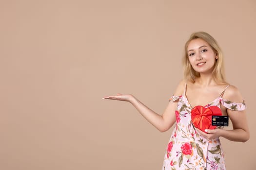 front view young female posing with red heart shaped present and bank card on brown background money equality sensual feminine march horizontal