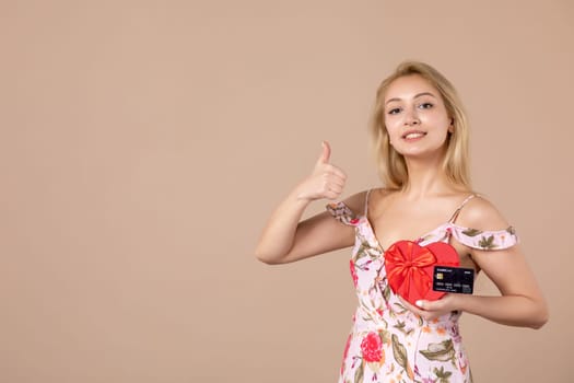 front view young female posing with red heart shaped present and bank card on brown background money sensual march horizontal woman equality