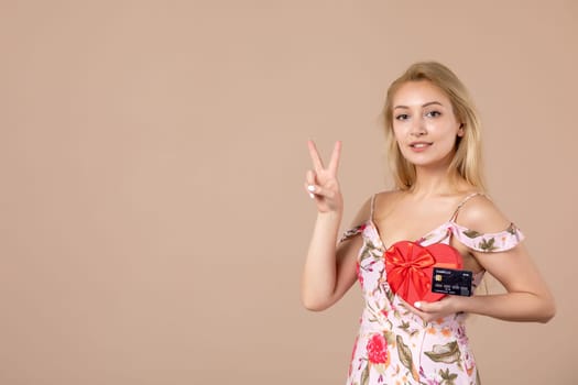 front view young female posing with red heart shaped present and bank card on brown background sensual march horizontal woman feminine equality