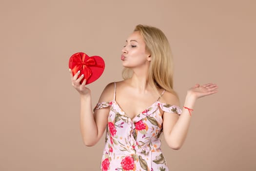 front view young female posing with red heart shaped present on brown background feminine sensual money march woman shopping equality horizontal