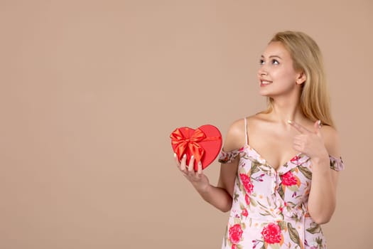 front view young female posing with red heart shaped present on brown background marriage feminine shopping money march horizontal equality woman