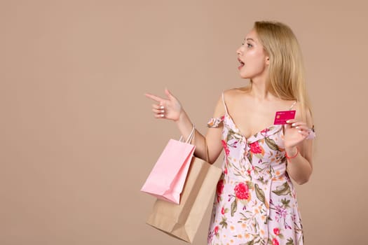 front view young female with present packages and bank card on brown background feminine sensual money march marriage woman shopping horizontal