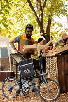 Organic locally grown fruits and vegetables delivery at farmers market, courier putting bio organic produce in thermal backpack and picking up order. Delivering food order fron local natural stand.