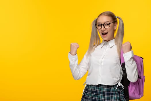 world book day happy cheering blonde schoolgirl with backpack on yellow background