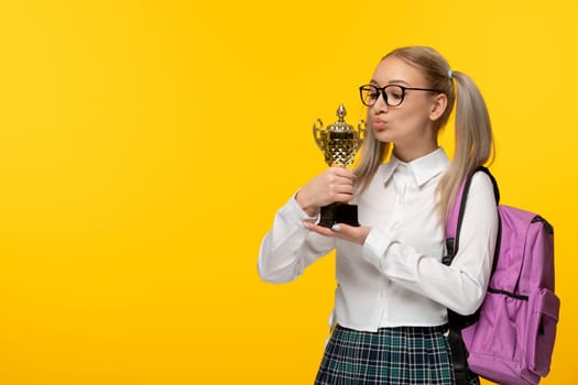 world book day a blonde cute schoolgirl in uniform kissing a golden trophy