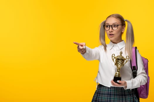 world book day blonde cute schoolgirl in uniform pointing left and holding a trophy