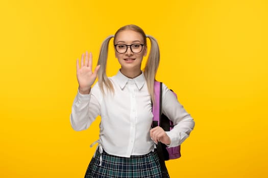 world book day blonde young school girl saying hi hand gesture smiling in glasses and uniform