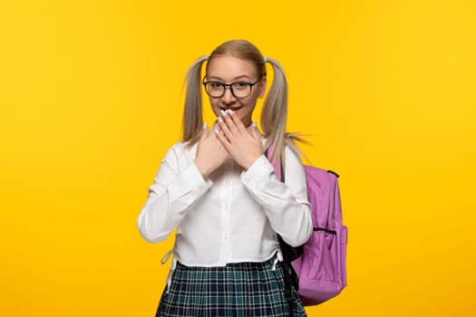 world book day cheerful blonde schoolgirl covering mouth smiling with pink backpack