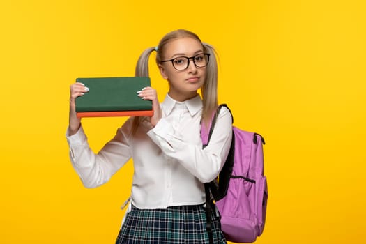 world book day serious blonde schoolgirl holding books and a pink backpack