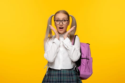 world book day surprised schoolgirl with ponytails hands under chin on yellow background