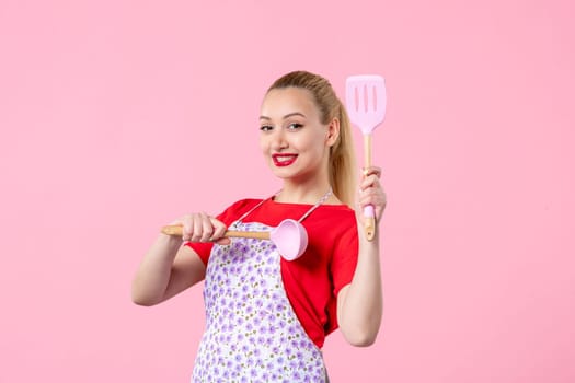 front view young pretty housewife in cape with spoons on pink background colors profession job uniform horizontal cooking worker