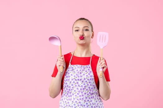 front view young pretty housewife in cape with spoons on pink background profession cooking worker uniform job color