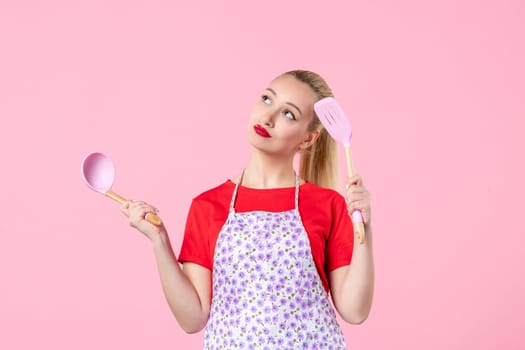 front view young pretty housewife in cape with spoons on pink background profession horizontal cooking uniform job color