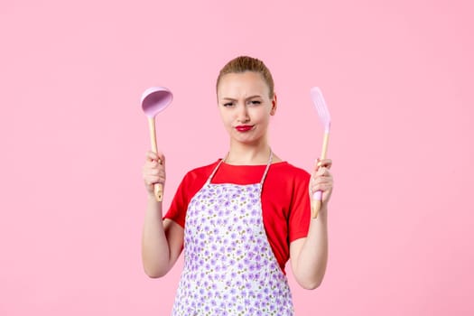 front view young pretty housewife in cape with spoons on pink background uniform duty job profession cooking wife horizontal occupation